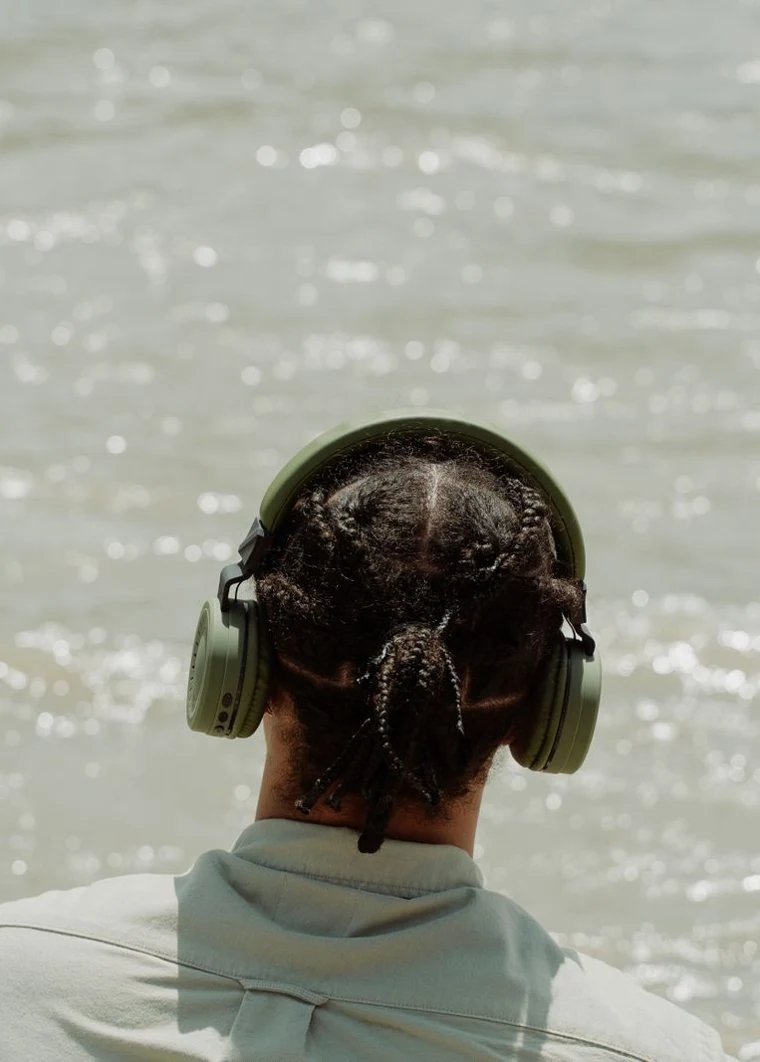 A listener wearing headphones beside sunlit water
